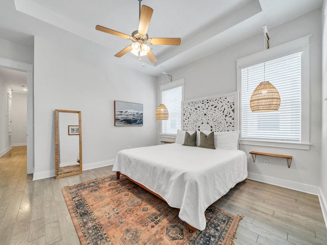 bedroom with a raised ceiling, ceiling fan, and light hardwood / wood-style floors