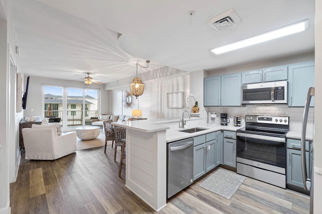 kitchen featuring backsplash, kitchen peninsula, sink, appliances with stainless steel finishes, and wood-type flooring