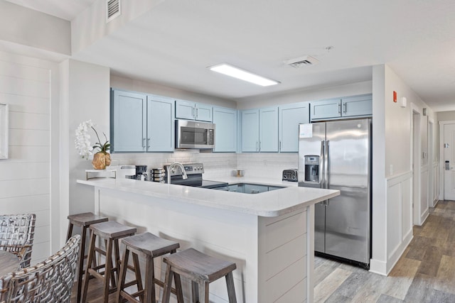 kitchen with a breakfast bar, backsplash, light hardwood / wood-style flooring, appliances with stainless steel finishes, and kitchen peninsula