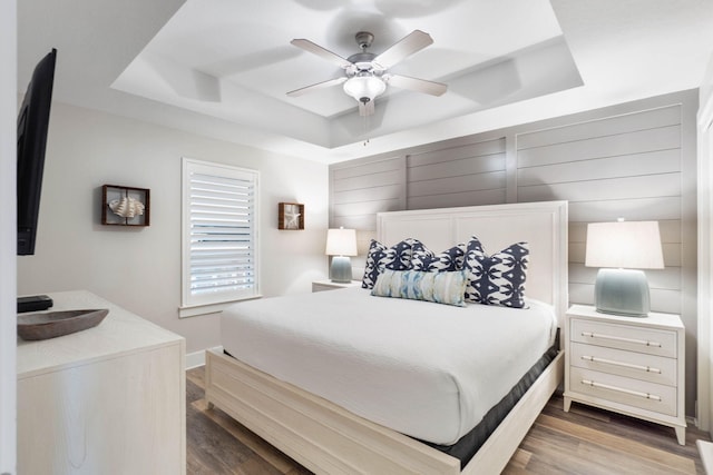 bedroom with a tray ceiling, ceiling fan, and dark hardwood / wood-style flooring