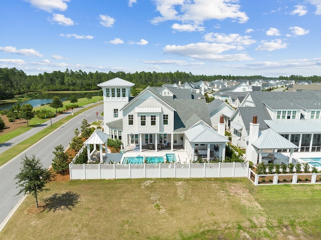 rear view of property featuring a water view, a patio area, a fenced in pool, and a lawn