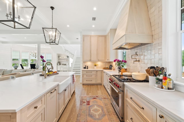 kitchen featuring high end stainless steel range, premium range hood, sink, crown molding, and light hardwood / wood-style floors