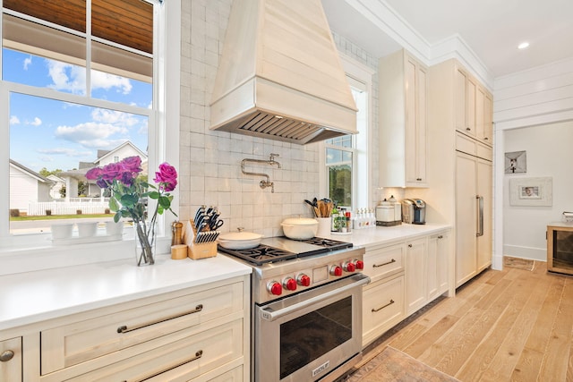 kitchen featuring custom range hood, a healthy amount of sunlight, light wood-type flooring, and luxury stove