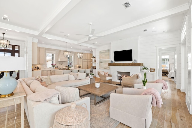 living room with a wealth of natural light, beamed ceiling, ceiling fan with notable chandelier, and light wood-type flooring