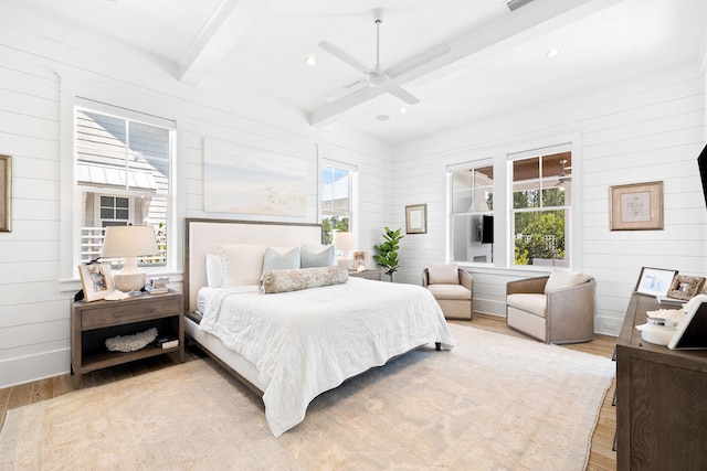 bedroom with ceiling fan, wooden walls, beamed ceiling, and light hardwood / wood-style floors