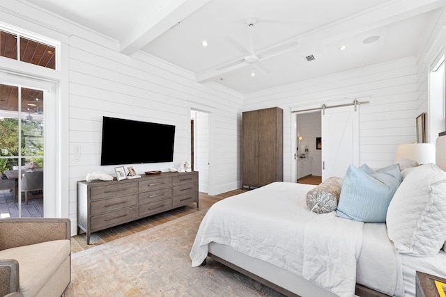 bedroom with ceiling fan, beam ceiling, a barn door, hardwood / wood-style flooring, and wood walls