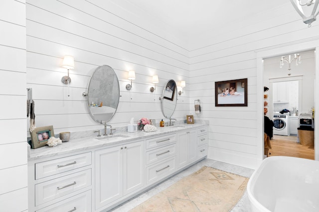 bathroom featuring a bath, washer / dryer, vanity, and wood walls