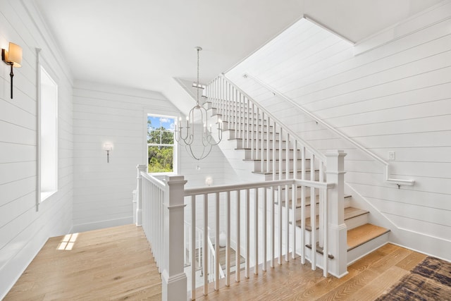 stairs with a chandelier, wood walls, and wood-type flooring