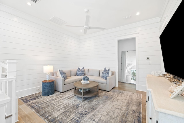 living room with hardwood / wood-style floors, ceiling fan, crown molding, and wood walls