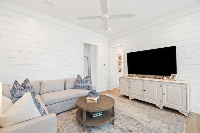 living room with light wood-type flooring, crown molding, ceiling fan, and wooden walls