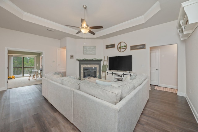 living room with a raised ceiling, crown molding, dark hardwood / wood-style flooring, and ceiling fan