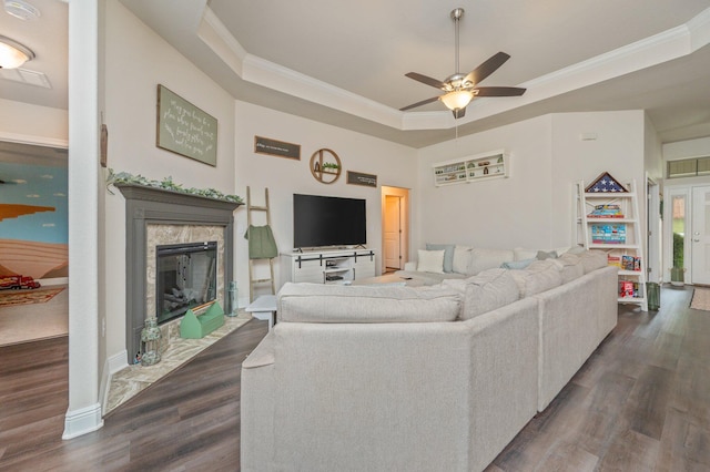 living room featuring ceiling fan, a premium fireplace, dark hardwood / wood-style floors, crown molding, and a tray ceiling