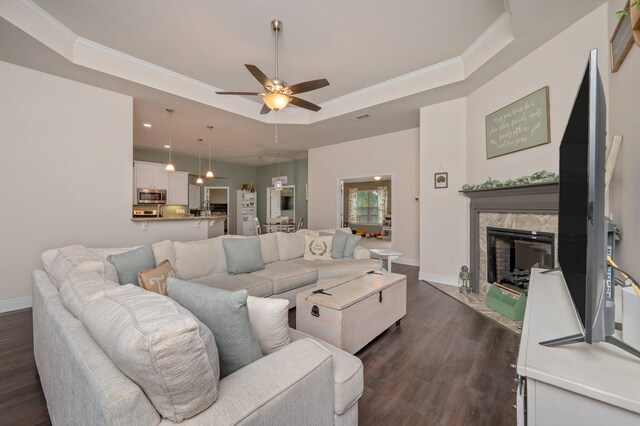 living room featuring ceiling fan, a premium fireplace, dark hardwood / wood-style flooring, a tray ceiling, and ornamental molding