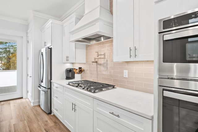 kitchen featuring light hardwood / wood-style floors, white cabinetry, appliances with stainless steel finishes, light stone countertops, and custom exhaust hood