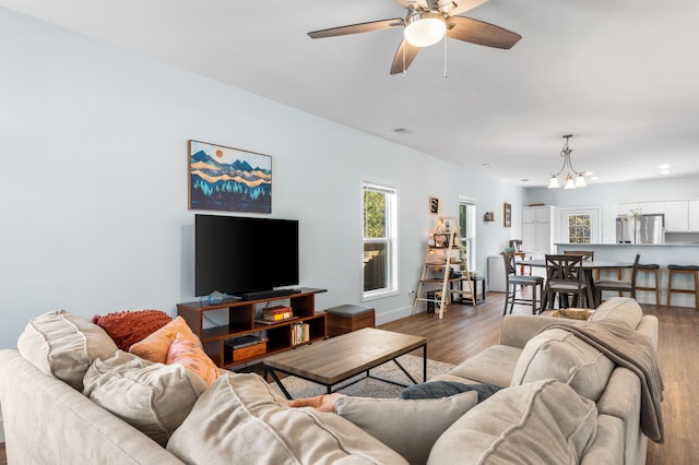 living area with ceiling fan with notable chandelier, wood finished floors, and baseboards