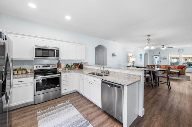 kitchen with appliances with stainless steel finishes, open floor plan, white cabinetry, a sink, and a peninsula