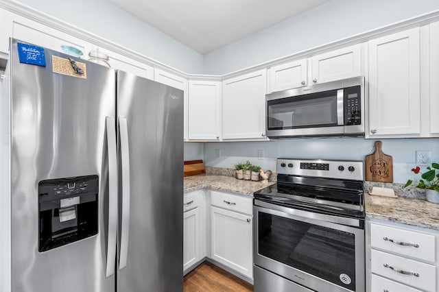 kitchen with stainless steel appliances, light stone countertops, white cabinetry, and light wood-type flooring