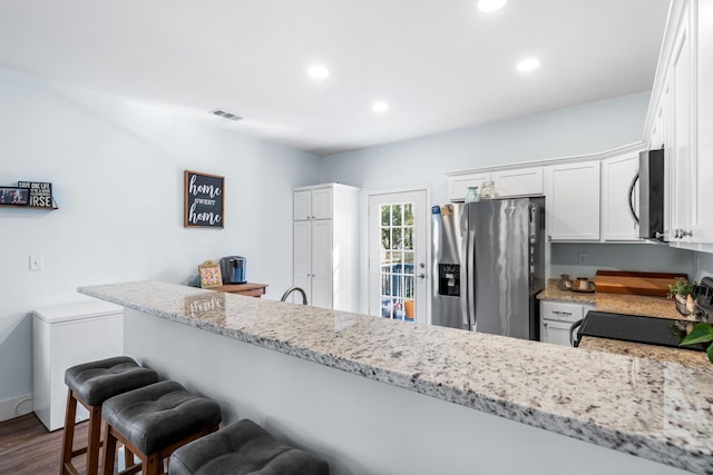 kitchen with light stone counters, stainless steel appliances, dark wood-type flooring, a peninsula, and white cabinetry