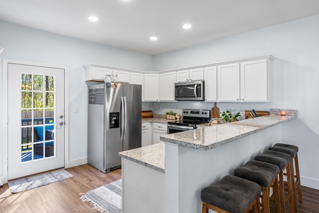 kitchen with light hardwood / wood-style floors, light stone counters, kitchen peninsula, white cabinetry, and appliances with stainless steel finishes