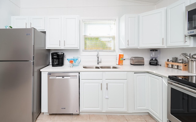 kitchen featuring white cabinetry, sink, appliances with stainless steel finishes, light tile patterned flooring, and ornamental molding