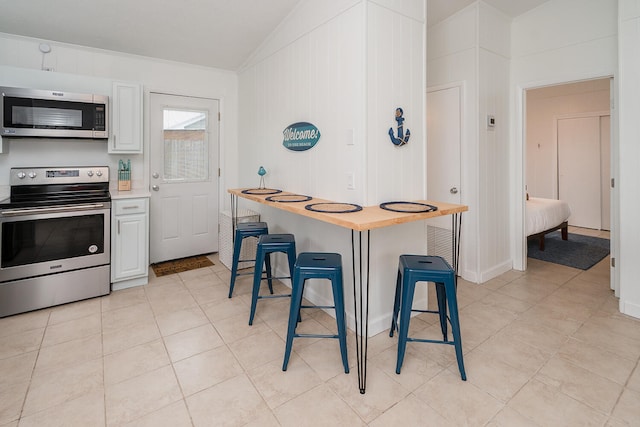 kitchen featuring a kitchen bar, stainless steel appliances, vaulted ceiling, light tile patterned floors, and white cabinetry