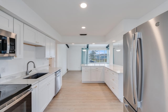 kitchen with white cabinetry, sink, stainless steel appliances, light hardwood / wood-style floors, and decorative light fixtures