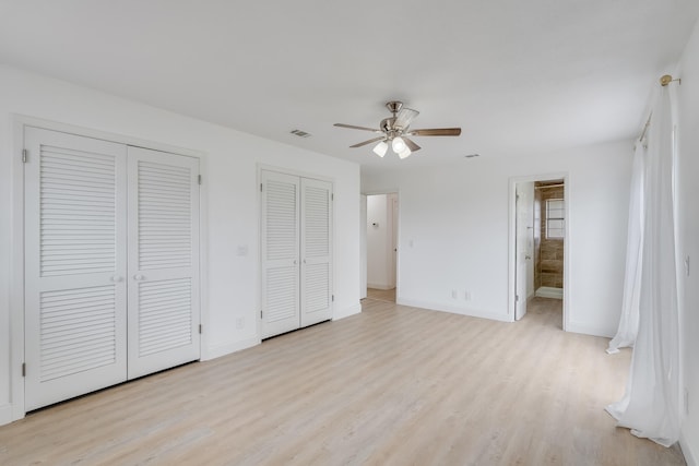 unfurnished bedroom featuring light wood-type flooring, two closets, ensuite bath, and ceiling fan