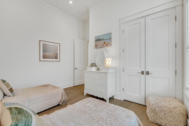 bedroom featuring light wood-type flooring, crown molding, and a closet