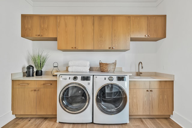 laundry room featuring cabinets, washing machine and dryer, light wood-type flooring, and sink