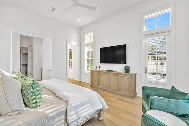 bedroom with a walk in closet, ceiling fan, light hardwood / wood-style floors, and ornamental molding