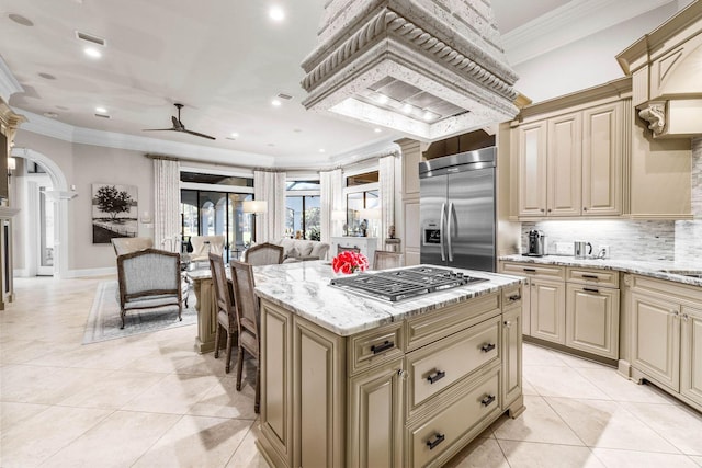 kitchen with light stone countertops, a center island, ceiling fan, stainless steel appliances, and crown molding