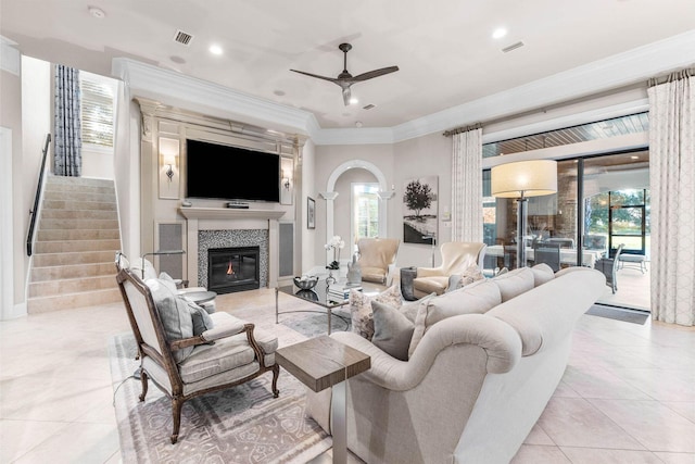 living room with ceiling fan, ornamental molding, a fireplace, and light tile patterned floors