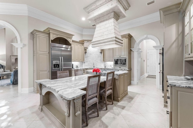 kitchen with built in appliances, a kitchen island, light stone counters, and ornate columns