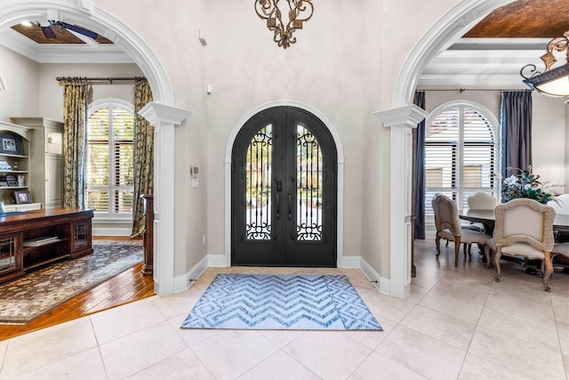 foyer with light wood-type flooring, crown molding, a wealth of natural light, and french doors