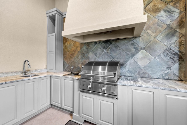 kitchen featuring light stone counters, sink, backsplash, and range hood