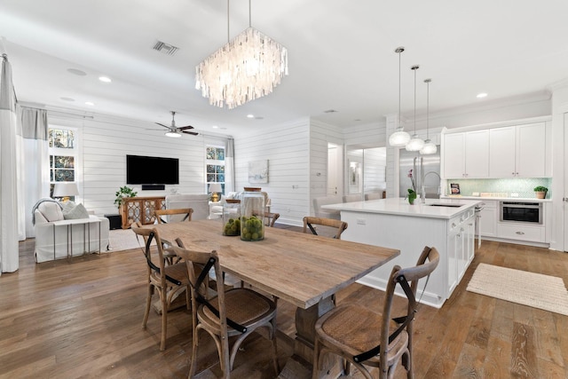 dining room featuring dark wood-type flooring, ceiling fan with notable chandelier, sink, wooden walls, and crown molding