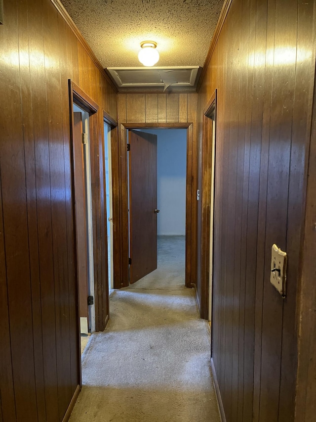 corridor with light carpet, a textured ceiling, and wooden walls