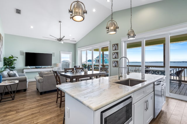 kitchen featuring stainless steel microwave, white cabinetry, a kitchen island with sink, light stone countertops, and a water view