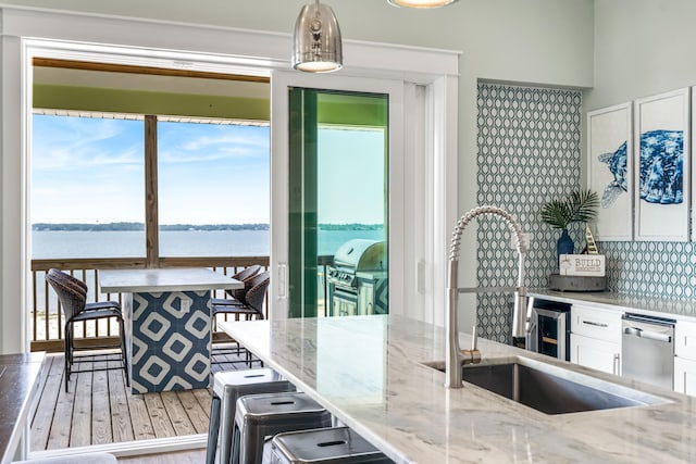 kitchen featuring pendant lighting, white cabinetry, tasteful backsplash, a water view, and light stone counters