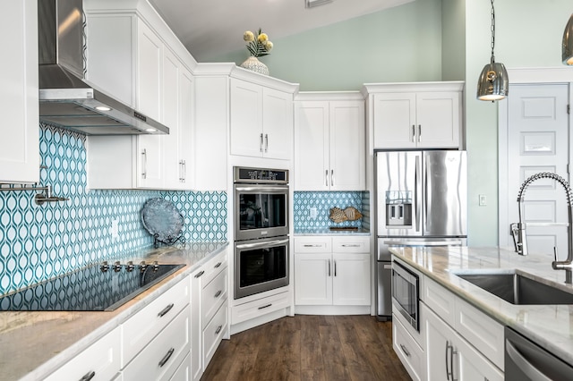 kitchen with stainless steel appliances, wall chimney exhaust hood, white cabinets, and light stone countertops