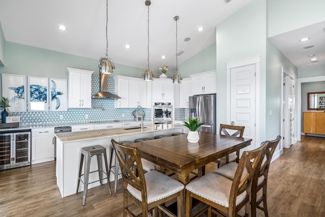 kitchen featuring stainless steel appliances, a kitchen island with sink, decorative light fixtures, beverage cooler, and white cabinets