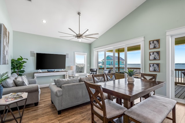 dining area with ceiling fan, a water view, wood-type flooring, and high vaulted ceiling