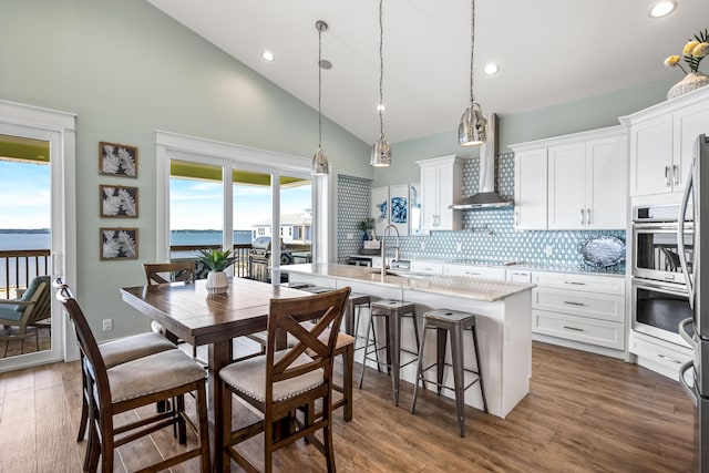 kitchen with backsplash, a kitchen island with sink, a water view, white cabinets, and wall chimney exhaust hood