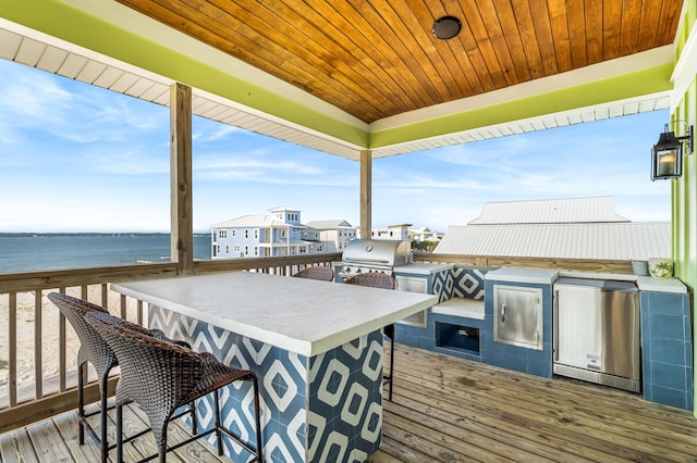 wooden deck with a water view, an outdoor kitchen, an outdoor bar, and area for grilling