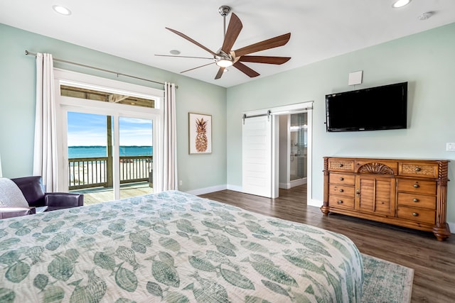 bedroom featuring ceiling fan, a barn door, access to exterior, a water view, and dark hardwood / wood-style flooring