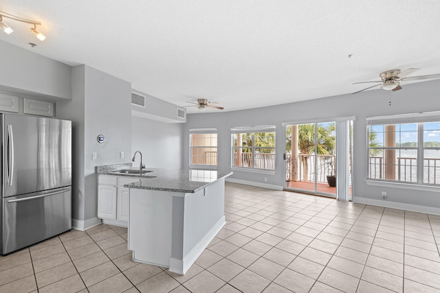 kitchen featuring kitchen peninsula, stainless steel fridge, light stone counters, sink, and light tile patterned flooring