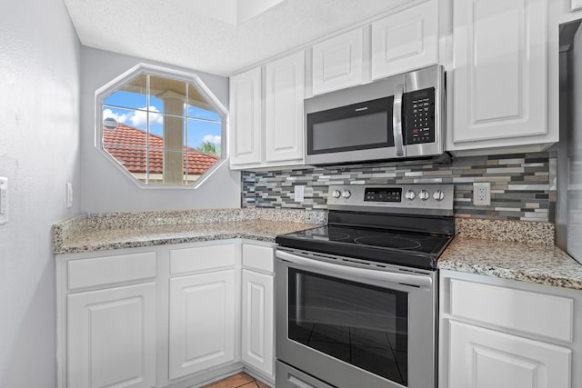 kitchen featuring white cabinets, light stone counters, backsplash, and appliances with stainless steel finishes