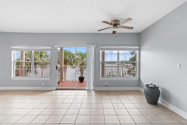 empty room with ceiling fan, light tile patterned flooring, and a textured ceiling