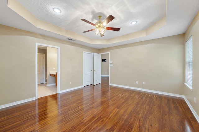 spare room with dark hardwood / wood-style floors, a raised ceiling, a textured ceiling, and a wealth of natural light