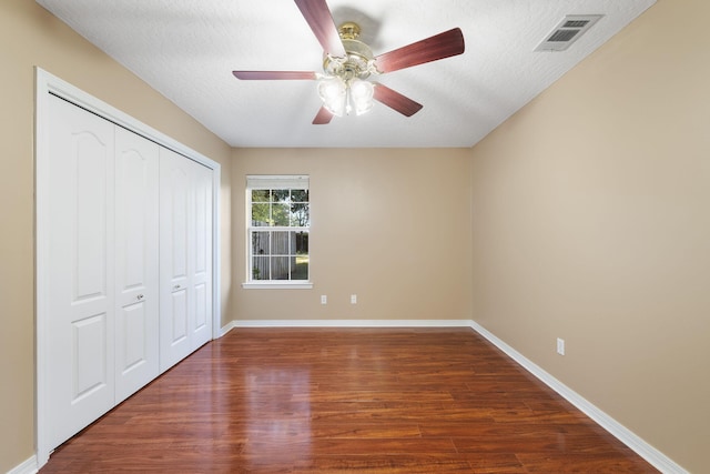 unfurnished bedroom with a textured ceiling, ceiling fan, dark wood-type flooring, and a closet